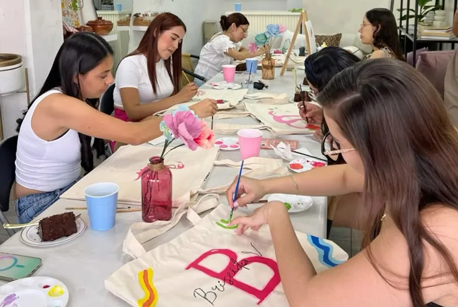 Women painting tote bags at a table.