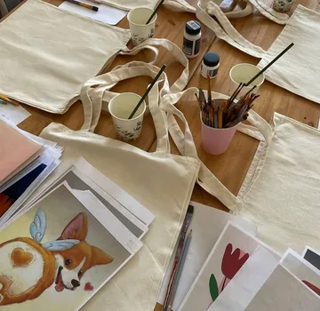 Tote bags, paintings, brushes on a wooden table.