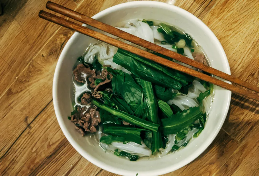 Bowl of pho with chopsticks on wood table.