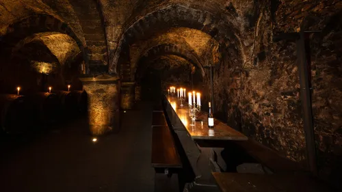 Candlelit wine cellar with wooden tables and barrels.