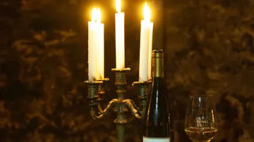 Kerzen brennen neben Weinflasche und Glas.