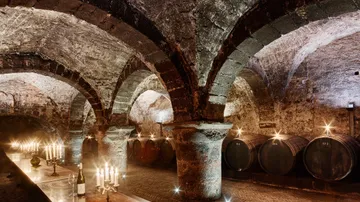 Wine cellar with tables, candlelight, and barrels.