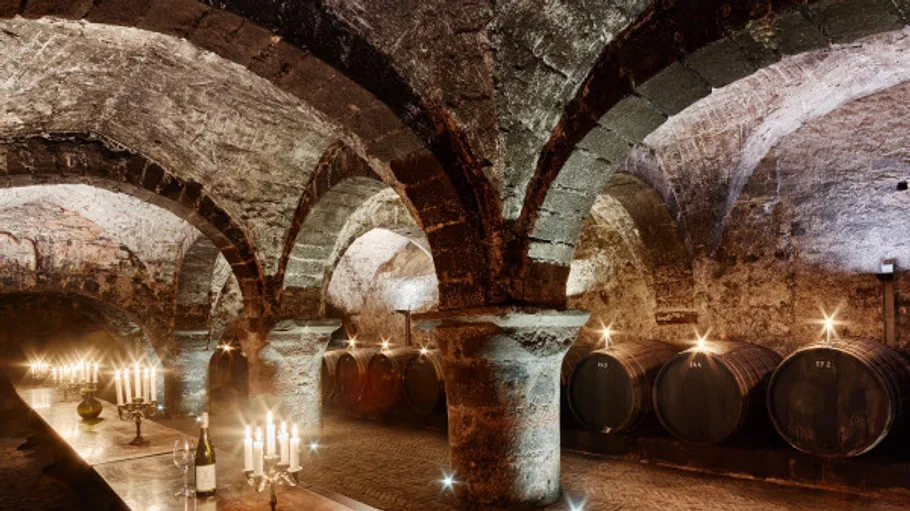 Wine cellar with tables, candlelight, and barrels.