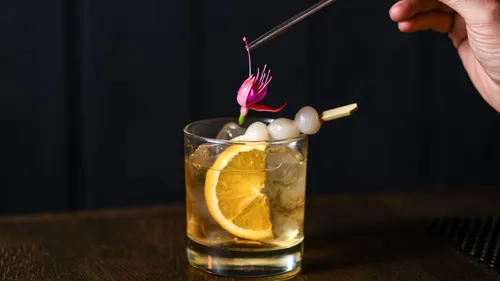 Hand garnishes cocktail with flower and ice.