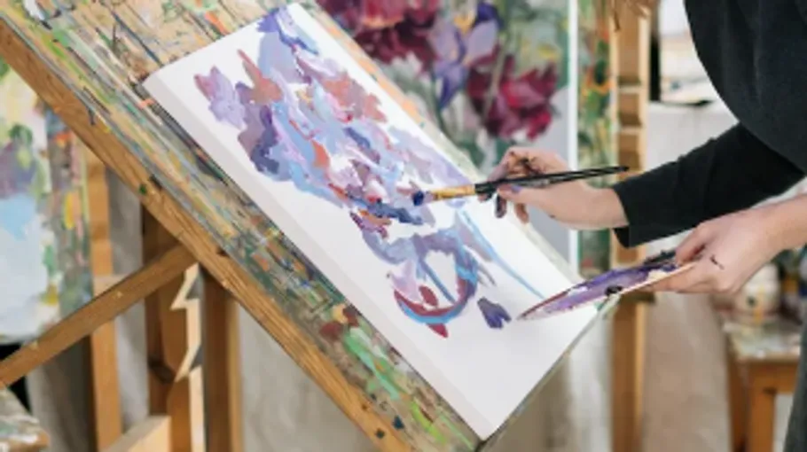 Person malt abstrakte Kunst auf Staffelei drinnen.