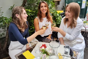 Drei Frauen stoßen an einem Gartentisch an.