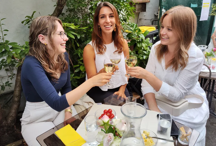 Three women clinking glasses at outdoor table.
