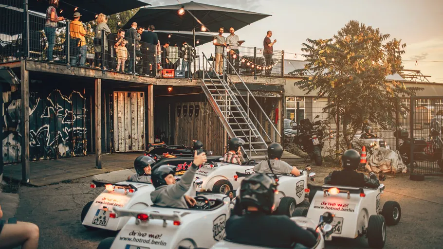 Small vehicles driving, people watching from balcony.