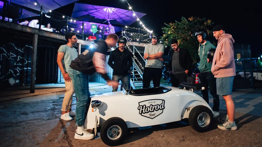 Group examining small white hotrod car at night.