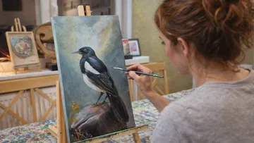 Woman painting a magpie in an art studio.