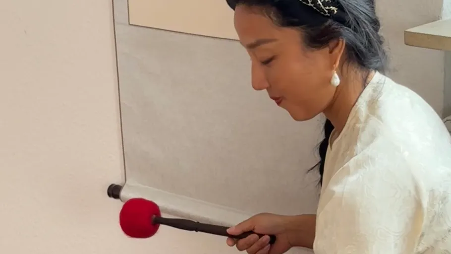 Woman painting with brush on scroll indoors.