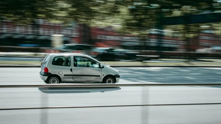 Small silver car driving on urban street.
