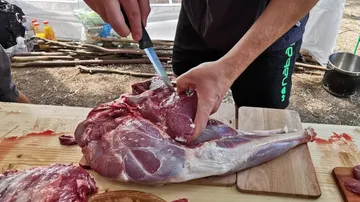 Person schneidet Fleisch auf einem Holztisch.