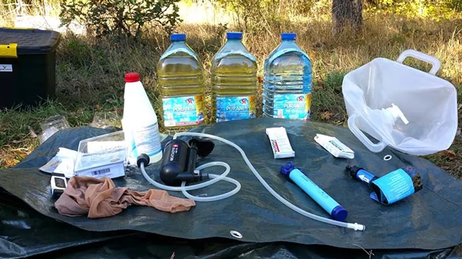 Campingausrüstung mit Wasser und Filtern auf Boden.