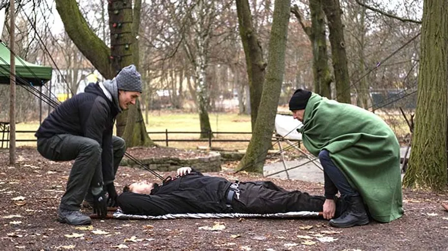 Zwei Personen heben Mann auf Trage im Freien.