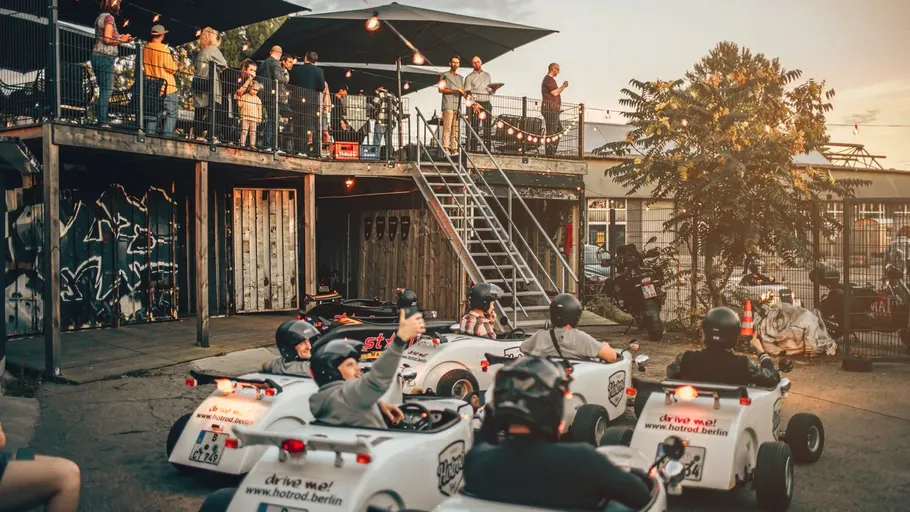 People driving mini hot rods, outdoor event, sunset.