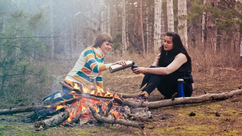Two people by a campfire in a forest.