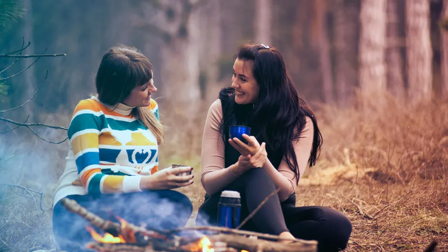 Two women talking by a campfire outdoors.