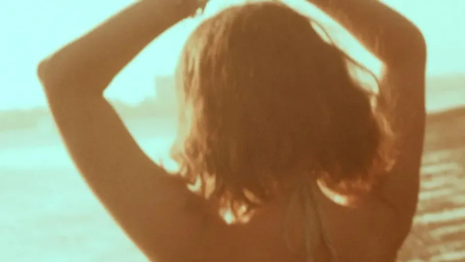 Person facing sea with arms raised.