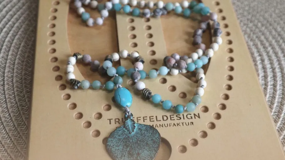 Beaded necklace with leaf pendant on a mat.