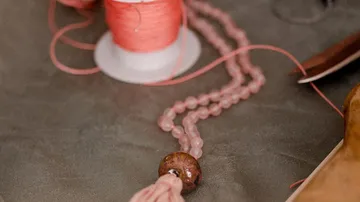 Rosa Perlen und Faden auf grauer Oberfläche.