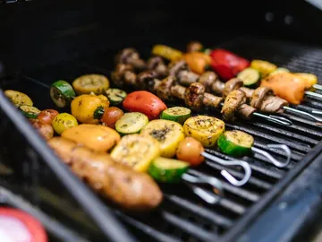 Gemüse und Spieße grillen auf einem Grillrost im Freien.