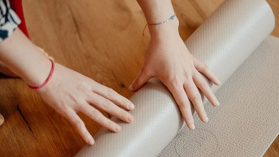Hände rollen Yogamatte auf dem Boden ein.