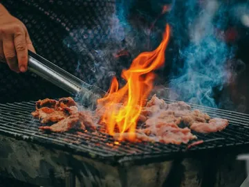 Meat is fried on the grill, flames and smoke are visible.