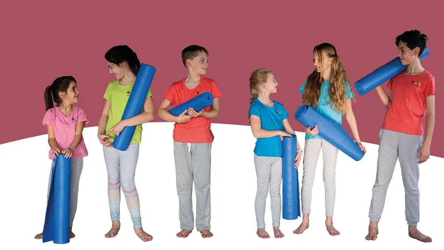 Group of kids holding yoga mats indoors.
