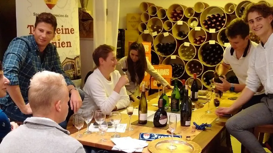 People tasting wine around a table, wine shelves behind.