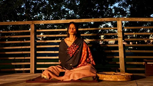 Person meditating on a wooden deck at sunset.