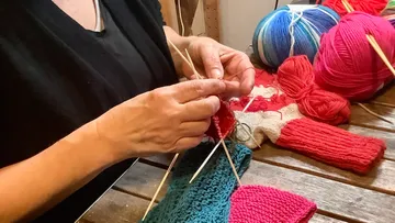 Person knitting with colorful yarn on table.