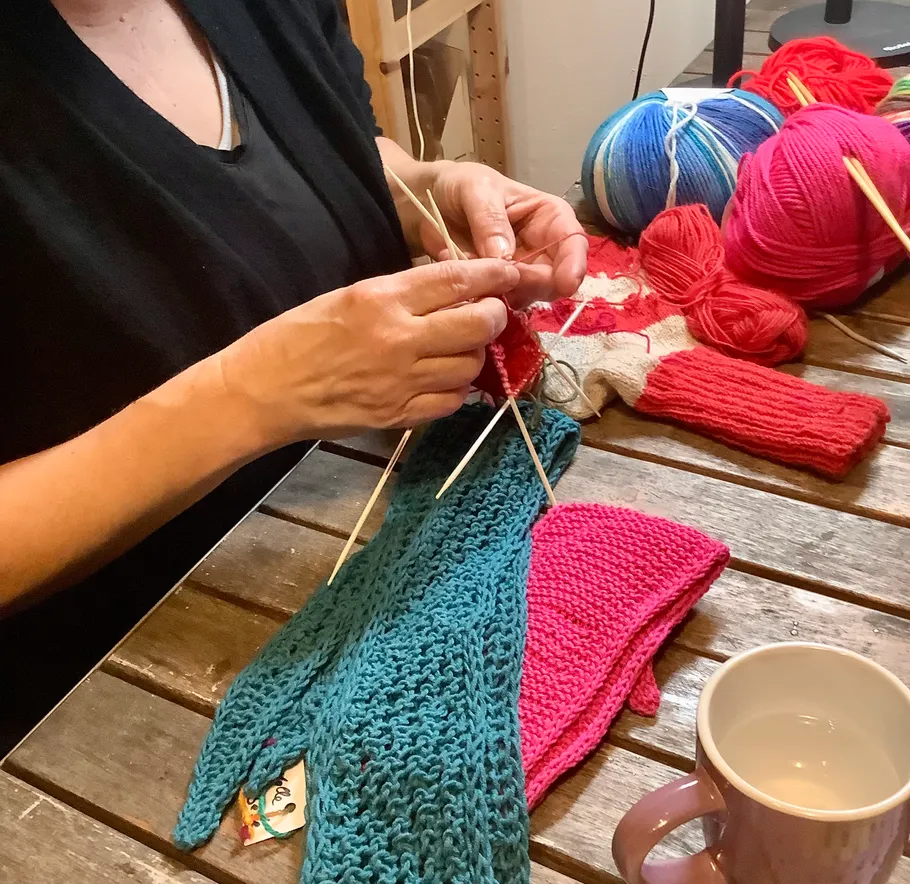 Person strickt mit buntem Garn auf Tisch.