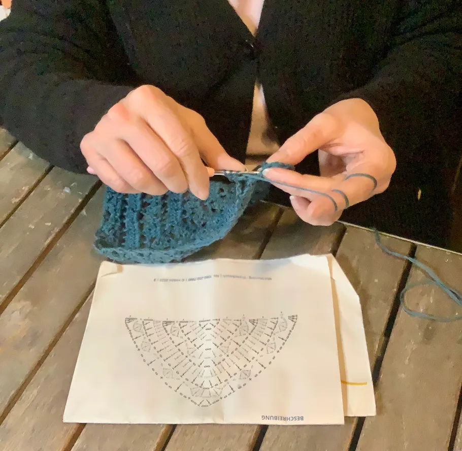 Person crocheting blue yarn at wooden table.