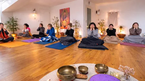Group meditating on mats indoors with bowls.