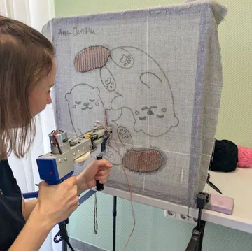 Person using tufting gun on otter design.