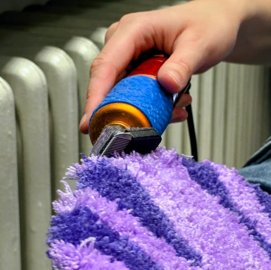 Hand using clipper on purple rug.