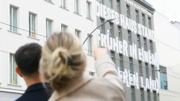 Personen zeigen auf Gebäude mit großem Text.