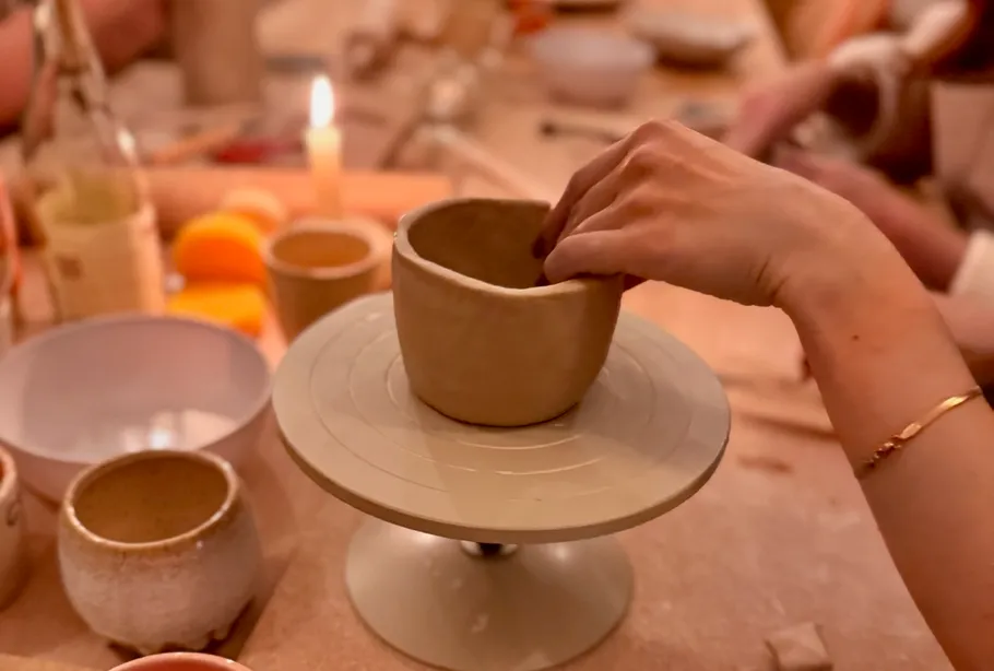 Person shapes clay bowl on pottery wheel.
