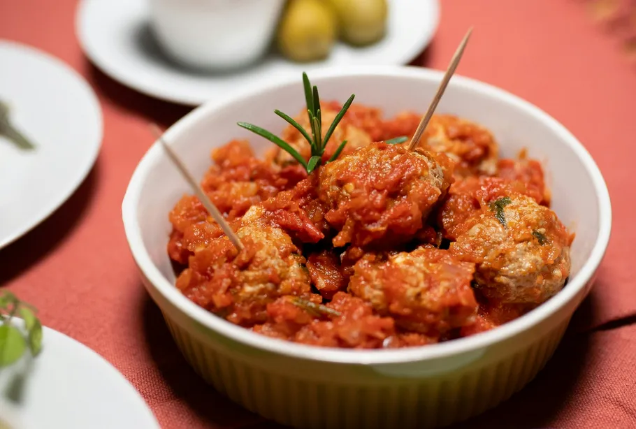 Fleischbällchen in Tomatensoße in weißer Schüssel.