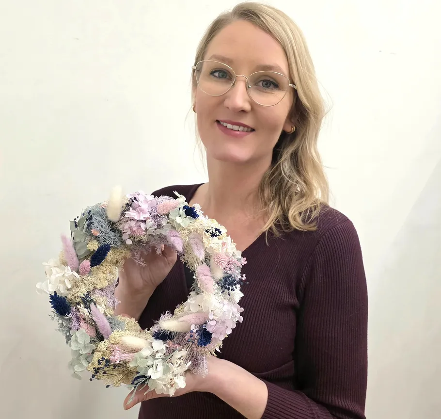 Woman holding a decorative floral wreath indoors.