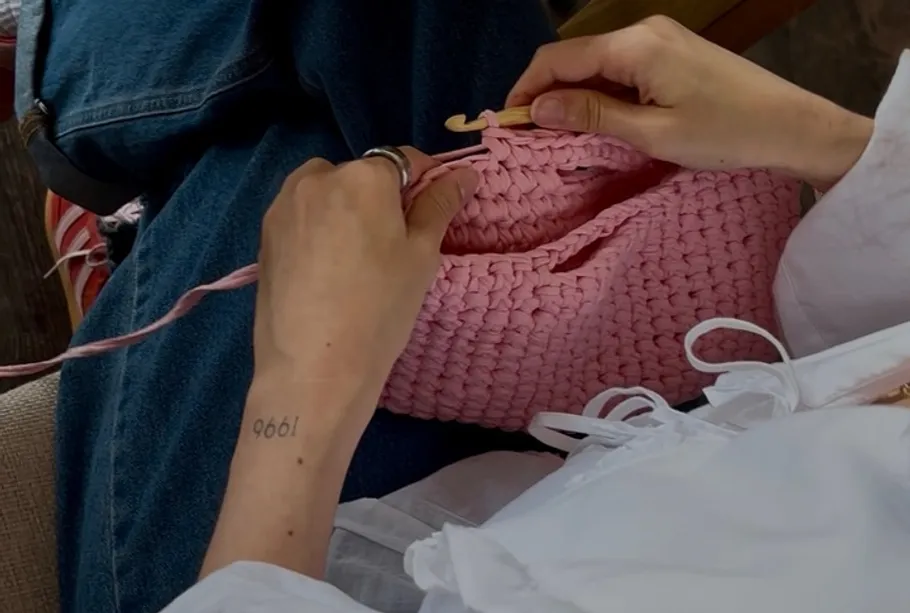 Person crocheting pink fabric on couch.