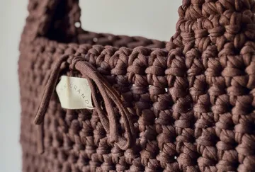 Braune geflochtene Tasche mit Griff und Etikett.