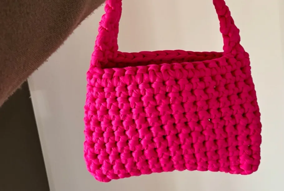 Pink crocheted handbag held close-up.