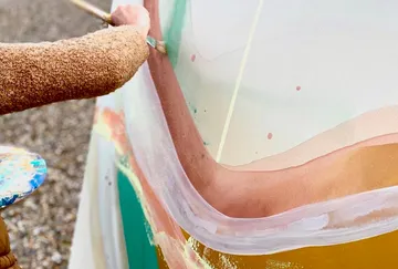 Person painting large colorful canvas outdoors.