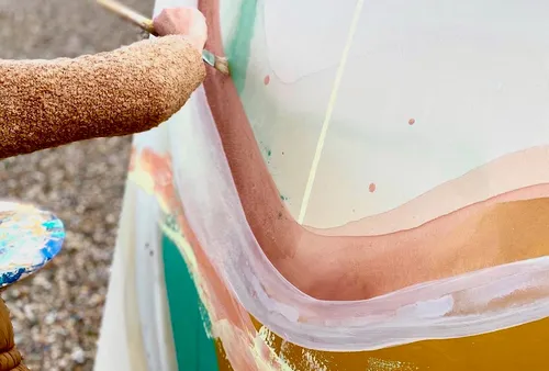 Person malt große bunte Leinwand im Freien.