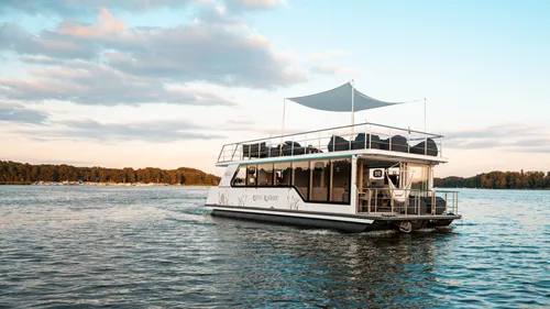 Houseboat cruising on calm lake at sunset.