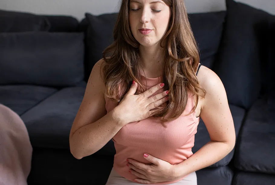 Woman meditating on sofa, hands on chest.