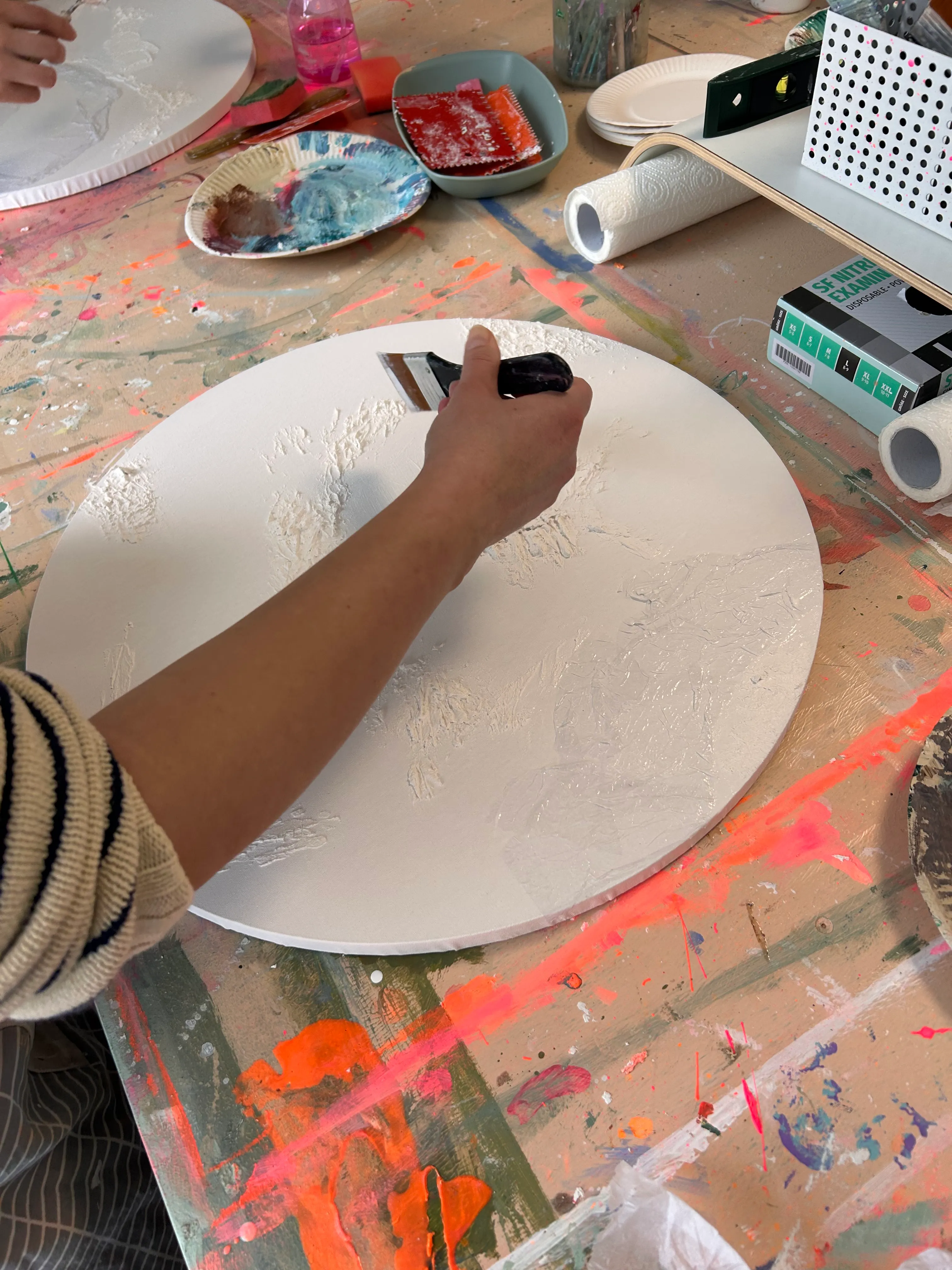 Person applies texture paste on round canvas.