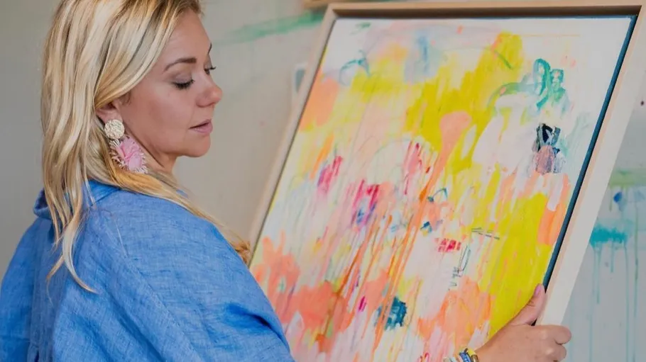 Woman holding colorful abstract painting in studio.